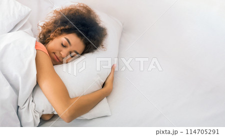 Relaxed african-american woman sleeping on bed and hugging pillow at home Relaxed african-american woman sleeping on bed and hugging pillow at home 114705291