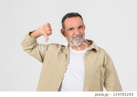 Disgruntled older man with a beard giving a thumbs down sign, signifying disapproval or dissatisfaction on white backdrop 114705293