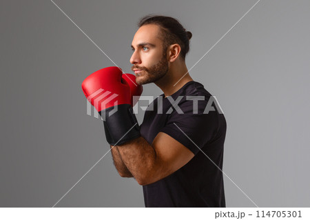 Serious man demonstrates readiness for a boxing session with a focused expression and gloves 114705301