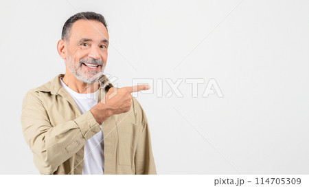 A cheerful elderly man with a beard smiles and points to the side, standing against a white background A cheerful elderly man with a beard smiles and points to the side, standing against a white background 114705309