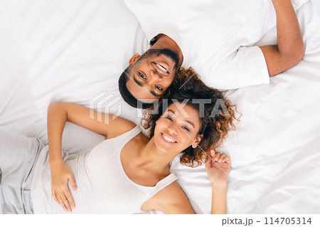 Enjoying every moment together. Top view on young loving black couple lying in bed together and looking at camera Enjoying every moment together. Top view on young loving black couple lying in bed together and looking at camera 114705314