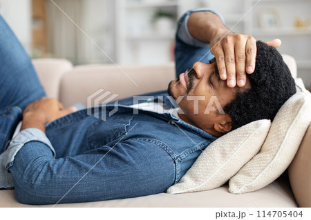 Black Man Feeling Unwell At Home, Suffering Stomach Pain And Headache, Upset African American Male Lying On Couch In Living Room, Closeup Black Man Feeling Unwell At Home, Suffering Stomach Pain And Headache, Upset African American Male Lying On Couch In Living Room, Closeup 114705404