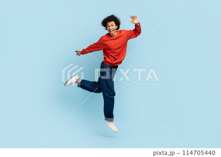 Joyful young african american man with curly hair jumping in mid-air expressing elation 114705440