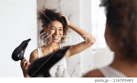 Smiling afro girl drying her hair in front of mirror in bathroom. 114705465