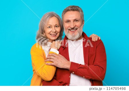 Marriage, happy partners. Portrait of mature man and woman sharing a tender moment, hugging and radiating happiness against blue studio background. Shot of loving senior couple 114705498