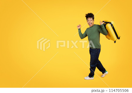 A delighted young african american man running and looking excited with a bright yellow suitcase on a vivid yellow background A delighted young african american man running and looking excited with a bright yellow suitcase on a vivid yellow background 114705506