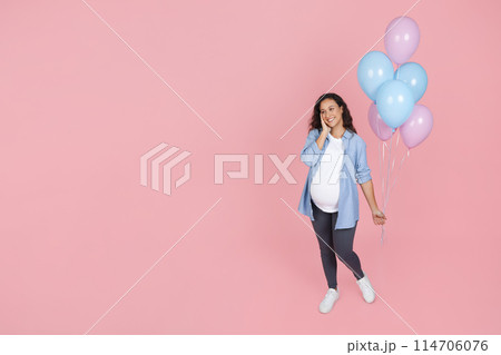 Boy or girl. Beautiful young expecting woman with big tummy attending gender reveal party, holding pink and blue balloons, touching her face and smiling, pink background, copy space 114706076