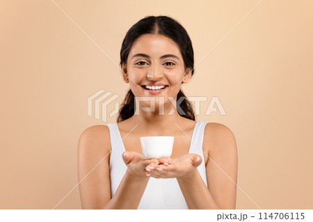 Best Cosmetics. Beautiful Young Indian Woman Holding Jar With Moisturising Cream And Smiling At Camera, Attractive Millennial Female In White Top Showing Beauty Product For Skincare, Copy Space 114706115
