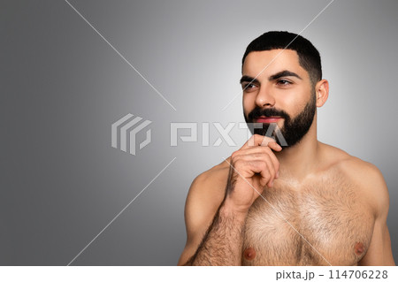 Beard grooming concept. Attractive millennial arab guy touching his nice beard and looking at copy blank space for advertisement, posing topless on grey studio background 114706228