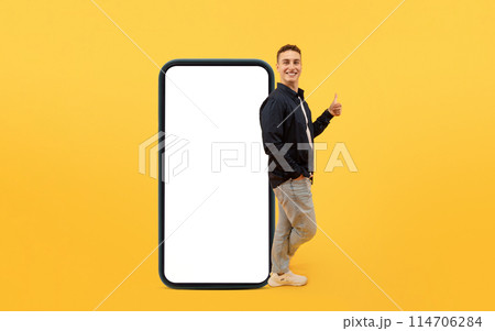 Cool young stylish european guy stand by big phone with white empty screen, showing thumb up and smiling at camera, recommend nice mobile app, mockup, copy space, yellow background Cool young stylish european guy stand by big phone with white empty screen, showing thumb up and smiling at camera, recommend nice mobile app, mockup, copy space, yellow background 114706284