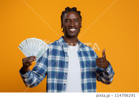 Great Profit. Happy Young Black Man Holding Dollar Cash Money And Showing Thumb Up, Smiling Handsome African American Millennial Guy Recommending Fast Credit, Standing On Yellow Studio Background 114706291