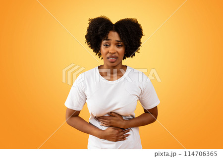 Food poisoning. Upset millennial african american woman with abdominal pain, suffering from diarrhea, touching her belly, isolated on colorful studio background Food poisoning. Upset millennial african american woman with abdominal pain, suffering from diarrhea, touching her belly, isolated on colorful studio background 114706365