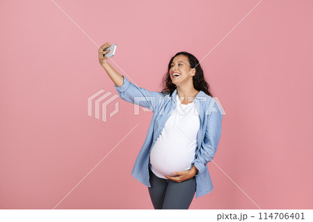 Happy beautiful young pregnant woman with big tummy taking selfie on smartphone, have video call with friends, influencer streaming isolated on pink background, prenatal blog Happy beautiful young pregnant woman with big tummy taking selfie on smartphone, have video call with friends, influencer streaming isolated on pink background, prenatal blog 114706401