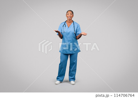 Smiling millennial black doctor surgeon, nurse in blue uniform, hold copy space on hands, spread hands to sides, isolated on gray studio background. Medical ad, offer, health care, professional choose Smiling millennial black doctor surgeon, nurse in blue uniform, hold copy space on hands, spread hands to sides, isolated on gray studio background. Medical ad, offer, health care, professional choose 114706764