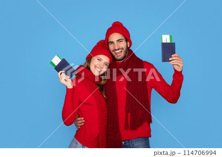 Travelling Concept. Young Smiling Couple Wearing Knitted Hats Holding Passports With Boarding Pass Tickets, Happy Man And Woman Ready For Winter Vacation, Posing Isolated On Blue Studio Background Travelling Concept. Young Smiling Couple Wearing Knitted Hats Holding Passports With Boarding Pass Tickets, Happy Man And Woman Ready For Winter Vacation, Posing Isolated On Blue Studio Background 114706994