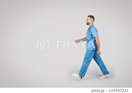 Dynamic side view of a male nurse in blue scrubs walking with purpose, depicting motion and active healthcare professional on the go, free space 114707231