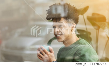 Shot from outside of happy stylish young black guy drinking coffee at cafe, holding green mug and looking at copy space, panorama. Leisure, millennials lifestyle concept Shot from outside of happy stylish young black guy drinking coffee at cafe, holding green mug and looking at copy space, panorama. Leisure, millennials lifestyle concept 114707233