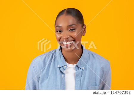 Headshot of pretty African American woman in denim shirt, confidently smiling over yellow studio backdrop. Modern fashion and female beauty concept, portrait for advertisement banner Headshot of pretty African American woman in denim shirt, confidently smiling over yellow studio backdrop. Modern fashion and female beauty concept, portrait for advertisement banner 114707398