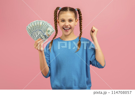 A young girl is seen holding a fan of money in her hand. She looks curious and excited as she grips the bills tightly. 114708057