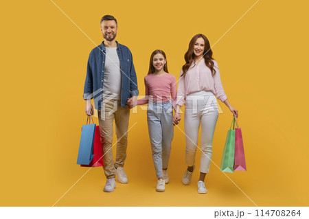 A happy family consisting of a father, mother, and their young daughter are walking side by side, holding colorful shopping bags A happy family consisting of a father, mother, and their young daughter are walking side by side, holding colorful shopping bags 114708264