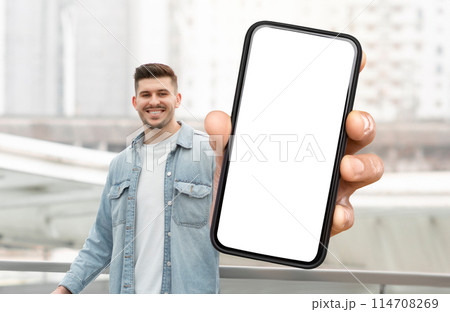 A man is holding a smart phone with white blank screen in his hand. The background is neutral, focusing on the man and the technology in his hand. A man is holding a smart phone with white blank screen in his hand. The background is neutral, focusing on the man and the technology in his hand. 114708269