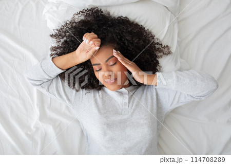 Hispanic woman is laying down in bed with her head resting in her hands, appearing contemplative or deep in thought, top view 114708289