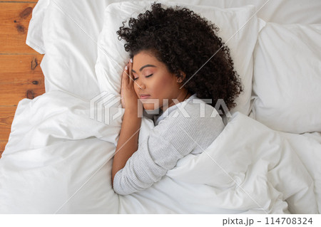 Pretty Hispanic woman is laying down on a bed, her head cradled in her hands. She appears to be deep in thought or contemplation, with a sense of introspection and reflection evident in her posture. 114708324
