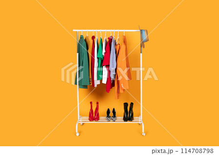 A rack filled with various clothing items is displayed against a vibrant yellow background. The clothes are neatly hung and arranged, showcasing different styles and colors ready for customers 114708798