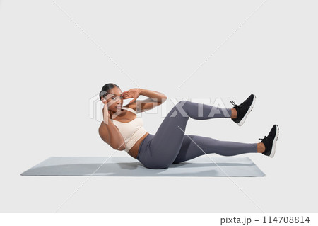 African American woman is actively engaging in an exercise routine on a mat. She is focused and demonstrating proper form while completing various movements to improve strength and flexibility. African American woman is actively engaging in an exercise routine on a mat. She is focused and demonstrating proper form while completing various movements to improve strength and flexibility. 114708814