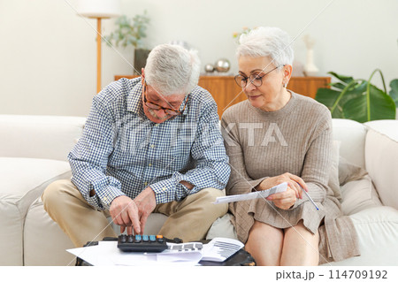 Middle aged senior couple sit with laptop and paper document. Older mature man woman reading paper bill pay online at home managing bank finances calculating taxes planning loan debt pension payment 114709192