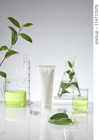 Mock up for advertising with a blank label tube in white color displayed on a glass pedestal in the middle of photo, a beaker, erlenmeyer and measuring cylinder in back over white background Mock up for advertising with a blank label tube in white color displayed on a glass pedestal in the middle of photo, a beaker, erlenmeyer and measuring cylinder in back over white background 114713976