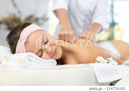 Female masseur works out shoulder and back problem area for female athlete client. Close-up 114716181