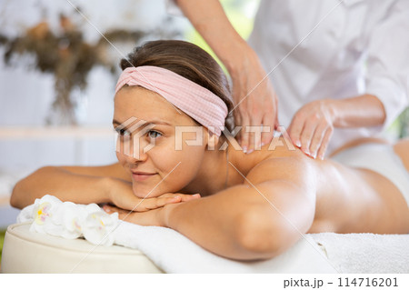 Young woman enjoying back and shoulders massage from professional masseuse 114716201