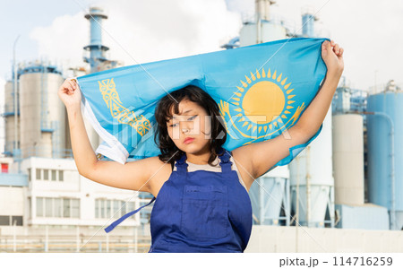 Worried asian girl in work clothes with flag of kazakhstan standing in front of industrial scenery 114716259