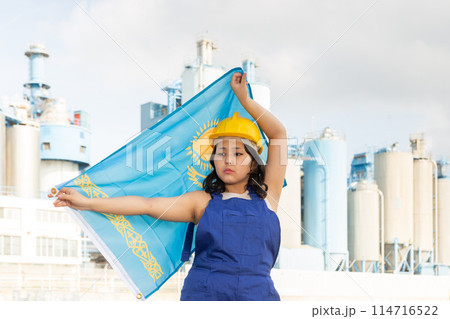 Upset girl in overalls with the Kazakhstan flag in her hands against the background of chimneys of modern factory Upset girl in overalls with the Kazakhstan flag in her hands against the background of chimneys of modern factory 114716522