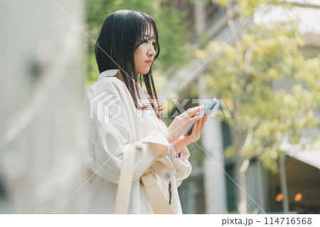待ち合わせ場所に友達が来なくて不安な若い女性がスマホに連絡が来ているか確認している場面のイメージ 114716568