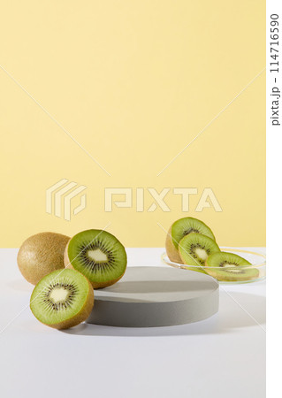 Gray podium in round shaped and some slices and halves of kiwi fruit are featured over pastel color background. Vacant space for presentation. Stage showcase on pedestal display 114716590