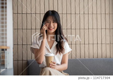 An attractive Asian businesswoman is talking on the phone while having a coffee break in a cafe. 114717304