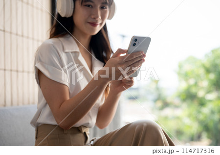 A cropped image of a woman is using her smartphone while listening to music on her headphones. 114717316