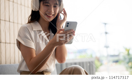 A cropped image of a woman is using her smartphone while listening to music on her headphones. 114717317