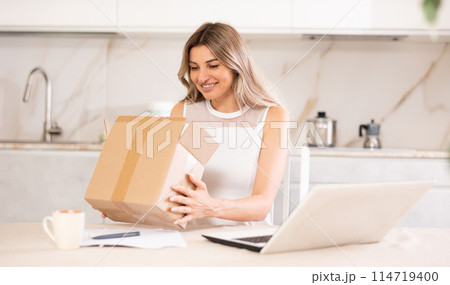 Happy girl unboxing cardboard delivery package at home Happy girl unboxing cardboard delivery package at home 114719400