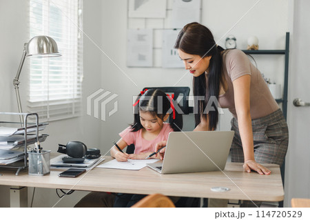 Mother helps daughter doing homework sitting at table writing in paper. Mother helps daughter doing homework sitting at table writing in paper. 114720529