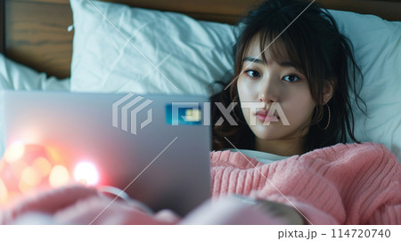 ノートパソコンとクレジットカードを持ってベッドに横たわる日本人女性 114720740