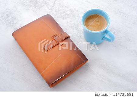 ミルクをたっぷり入れたコーヒーを飲みながら、茶色の革のシステム手帳でデスクワークをしているイメージ 114723681