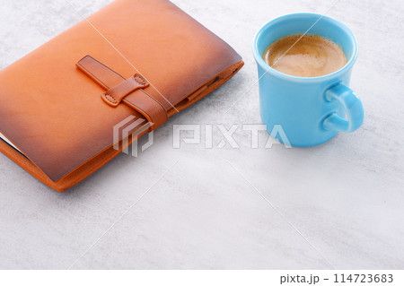 ミルクをたっぷり入れたコーヒーを飲みながら、茶色の革のシステム手帳でデスクワークをしているイメージ ミルクをたっぷり入れたコーヒーを飲みながら、茶色の革のシステム手帳でデスクワークをしているイメージ 114723683