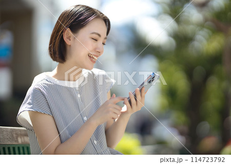 街中のベンチに座ってスマホを見る若い女性 街中のベンチに座ってスマホを見る若い女性 114723792