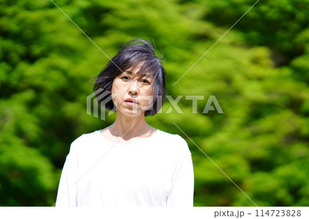 緑の中で白い服を着て寂し気に立つ中年女性 114723828