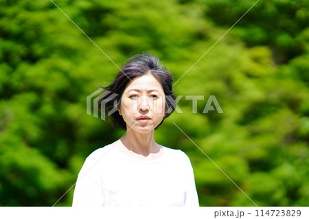 緑の中で白い服を着て寂し気に立つ中年女性 114723829