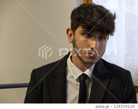 a sitted caucasian teenager in a business suit adjusts his white shirt a sitted caucasian teenager in a business suit adjusts his white shirt 114724129