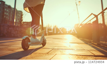 A girl rides a scooter along a city street flooded with sunlight. A girl rides a scooter along a city street flooded with sunlight. 114724934